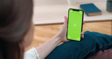 Kadının elinde tuttuğu ve akıllı telefonun yeşil ekranına baktığı arka plan görüntüsü. Sağır kadın evdeki kanepede otururken video görüşmesi yapıyor. İşitme kaybı kavramı.
