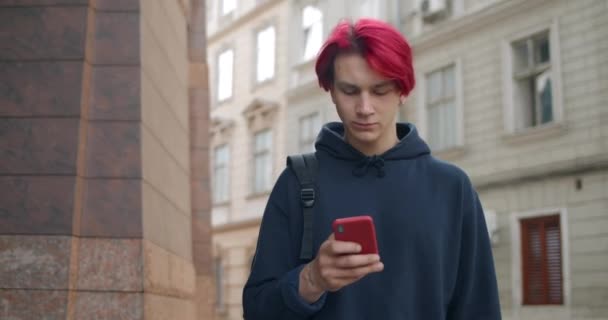 Crop view of millennial man in sweat à capuche en utilisant le téléphone portable tout en marchant dans la rue. Hipster mâle avec les cheveux roux teints défilement des médias sociaux fil d'actualité et de regarder l'écran. — Video