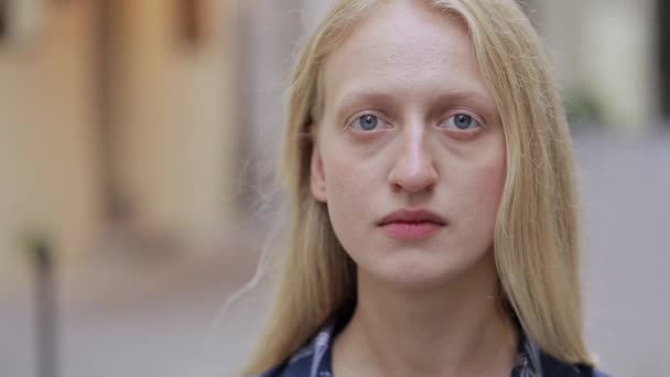 Vista de cerca de una mujer atractiva mirando a la cámara. Retrato de mujer de cabello rubio con ojos azules. Concepto de headshot.Blurred fondo. Al aire libre. — Vídeo de stock