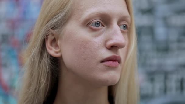 Närbild av sorgsen kvinna tittar åt sidan. Porträtt av blont hår kvinnlig person med blå ögon. Begreppet headshot. Suddig graffiti bakgrund. Utomhus. — Stockvideo
