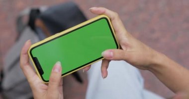Sokakta otururken internet oyunları oynamak için telefon kullanan bir kadın görüntüsü. Akıllı telefonu elinde tutan kadın şablon ekranını yatay ve dokunaklı olarak görüntüle.