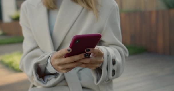 Schnittansicht einer stilvollen Frau, die auf dem Smartphone-Bildschirm tippt, während sie auf der Bank sitzt. Unbekannte Frau surft im Internet und verbringt Freizeit an der Stadtstraße. — Stockvideo