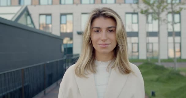 Vista de la cosecha de mujer segura atractiva con el pelo rubio mirando a la cámara. Elegante persona femenina sonriendo mientras camina por la calle de la ciudad. Concepto de estilo de vida. — Vídeo de stock