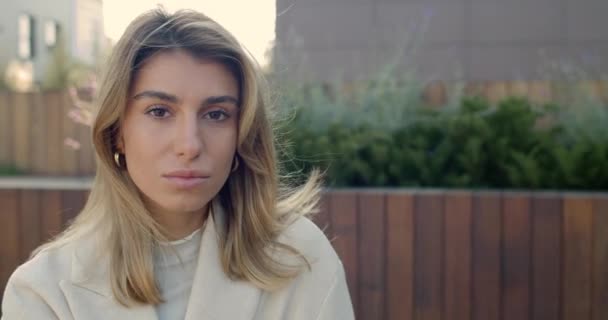 Close up view of attractive young woman looking aside and than to camera while wind blowing her blond hair. Portrait of charming female person smiling at street. — Stock Video