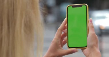 Bilinmeyen kadının iki eliyle akıllı telefon yeşil ekran tutarken üstten görünüşü. Açık havada boş sahte telefon kullanan kadın görüntüsünü kapat. Bulanık arkaplanda araç sürme.