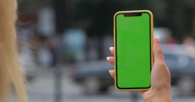 Sarışın kadının elinde tuttuğu ve akıllı telefon taklidi yaptığı bir manzara. Yeşil şablon ekranlı telefon kullanan kadın görüntüsü. Bulanık arkaplanda araç sürme.