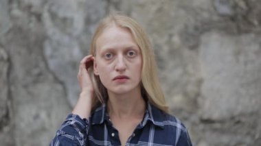 Mavi gömlek giyen, saçını okşayan ve kameraya bakan genç bir kadının portresi. Şehir caddesinde dikilen sarışın kadın görüntüsü. Vesikalık fotoğraf kavramı. Açık havada..