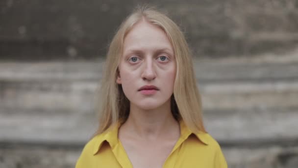 감정 이상 한 여자가 카메라를 보는 모습. 파란 눈에 금발의 슬픈 사람이 시가지에 서 있는 모습을 가까이서 볼 수있다. 헤드샷의 개념. 옥외에서. — 비디오