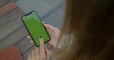 Caddedeki telefon ekranına bakan ve baskı yapan kadının omuz üstü görüntüsü. Takip noktaları olan akıllı telefon kullanan kadın görüntüsü. Krom anahtar kavramı, yeşil ekran.