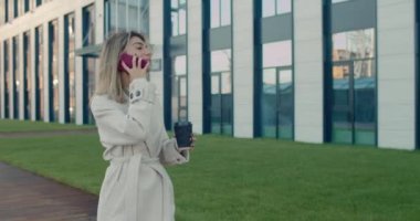Elinde kağıt kahve fincanı tutarken telefona gülümseyen kadın. Şehir caddesinde yürürken güzel bir kadın arkadaşıyla sohbet ediyor. İletişim kavramı.