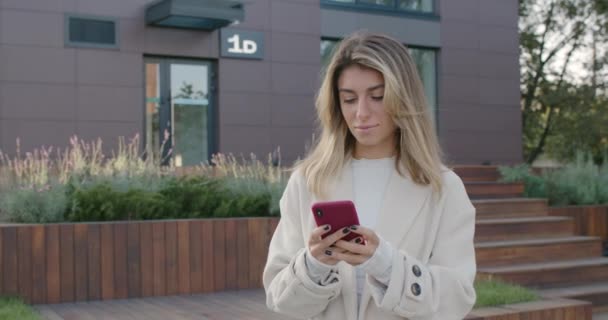 站在城市街道上用智能手机吸引女性的人。时尚的年轻女性在社交媒体上一边打字一边微笑。交流的概念. — 图库视频影像