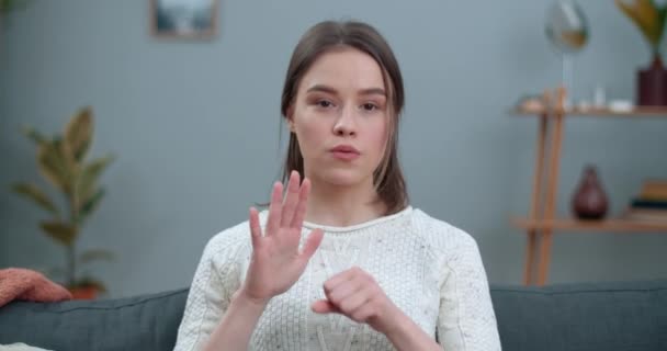 Close up view of woman showing with deaf-mute sign language stop animal abuse while sitting on sofa. Female pretty person supporting animal protection movement while sitting on sofa. — Stock Video