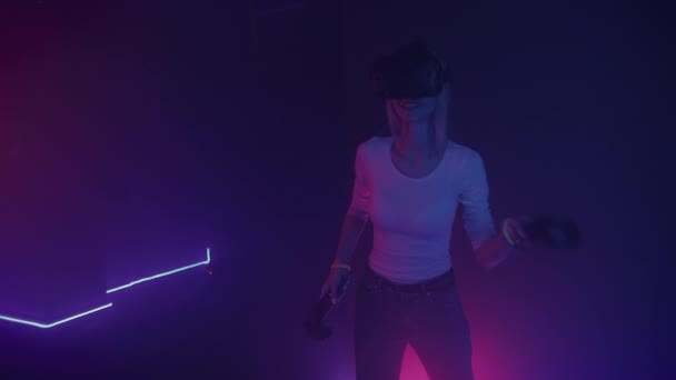 Молодая счастливая девушка в наушниках виртуальной реальности держит джойстик контроллеры играть в игру, глядя взволнован на фоне абстрактного неонового освещения. Мбаппе, Развлечения. — стоковое видео