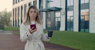 Sarı saçlı, akıllı telefon kullanan, kağıt kahve fincanı taşıyan çekici bir kadın. Başarılı bir kadın sokakta yürürken sesli mesaj yazdırıyor..
