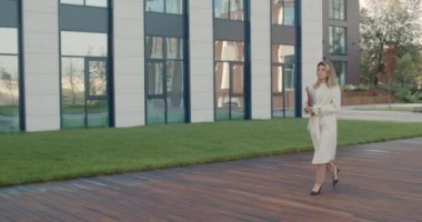 Deri çantalı ve akıllı telefonlu kendine güvenen bir iş kadınının yan görüntüsü. Şehir caddesinde yürüyen kendinden emin genç bir kadın. Başarılı insanlar kavramı.