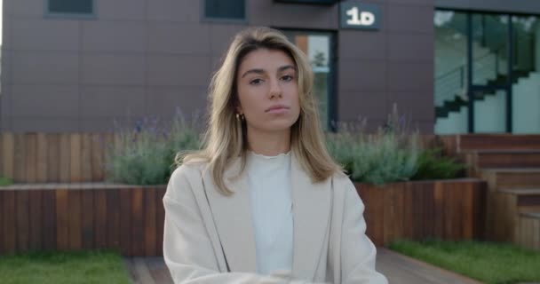 Retrato de mujer hermosa con el pelo rubio girando la cabeza y mirando a la cámara. Vista de la cosecha de atractiva persona femenina cruzando los brazos mientras está de pie y posando en la calle. Al aire libre. — Vídeos de Stock