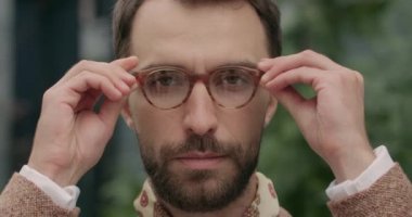 Ciddi sakallı, şık bir atkısı olan ve kameraya bakan bir adamın portresi. Şehir caddesinde dikilirken gözlüklü yakışıklı bir adama yaklaş. Vesikalık fotoğraf kavramı.