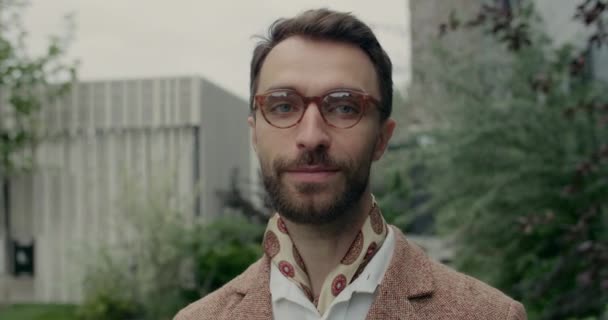 Vista de cerca del hombre guapo con la barba mirando y sonriendo a la cámara. Retrato de un tipo elegante girando la cabeza y de pie en la calle. Concepto de estilo de vida, headshot. — Vídeo de stock