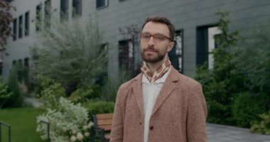 Kendine güveni tam, gözlüklü, başını çevirip kollarını kavuşturan erkek portresi. Şehir caddesinde dikilirken şık giyinen yakışıklı sakallı adam..