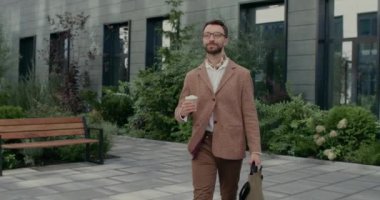 Poşet ve kahve fincanı taşıyan gözlüklü yakışıklı bir adam. Şehir caddesinde yürürken takım elbiseli, sakallı iş adamı gülümsüyor. Başarı kavramı.