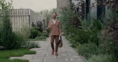 Çanta ve kahve bardağı taşırken mutlu atlayan gözlüklü yakışıklı adam. Fularlı neşeli sakallı adam sokakta yürürken seviniyor ve gülümsüyor. Başarı kavramı.