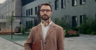 Kameraya bakarken ceketini ayarlayan gözlüklü yakışıklı adamın portresi. Kravat ve takım elbiseli sakallı adam sokakta dikilirken deri klasör tutuyor. Başarı kavramı.
