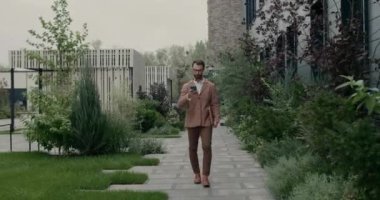 Şık giyinmiş, akıllı telefon kullanıp gülümseyen neşeli bir adam. Gözlüklü yakışıklı işadamı telefon ekranını kaydırıyor ve şehir caddesinde yürürken deri klasör tutuyor..