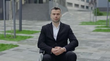 Şehir caddesinde tekerlekli sandalyede oturan ciddi bir erkek CEO idari takım elbisesinin ekili görüntüsü. 40 'lı yaşlarda kameraya poz veren ciddi engelli bir adamın portresi. Açık havada..