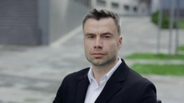 Kameraya bakan ciddi bir iş adamının yakın görüntüsü. 40 'lı yaşlarda takım elbiseli ve gömlekli düşünceli bir adamın portresi ofis binalarının yanında poz veriyor. İş kavramı.