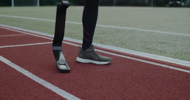 Crop view of disabled male person with prosthesis standing at sports field. Male sportsman with amputated leg getting ready to run. Concept of motivational sports footage. — Stock Video