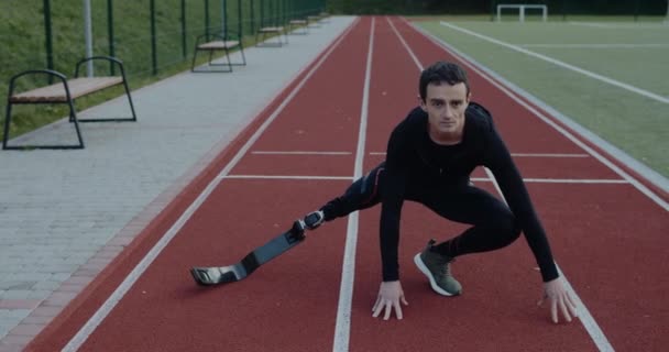 Stark ung manlig idrottsman med protes löparblad sträcker armar och ben på idrottsplanen. Man med amputerat ben gör övningar utomhus. Begreppet motiverande sportfilm. — Stockvideo