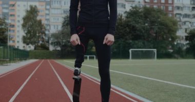 Spor sahasında duran protez koşu bıçaklı engelli adamın portresi. Genç, ampüte erkek koşucu dışarıda kameraya bakıyor. Motivasyon sporu görüntüsü kavramı.