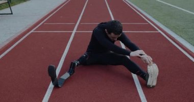 Spor sahasında otururken protez bıçakları olan engelli bir adam. Bacağı kesilmiş bir erkek ısınıyor ve dışarıda egzersiz yapıyor. Özürlü kavramı.