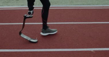 Spor sahasında yürüyen protez bıçaklı engelli erkek bacaklarının yan görüntüsü. Engelli erkek sporcu koşuya hazırlanıyor. Motivasyon sporu görüntüsü kavramı.