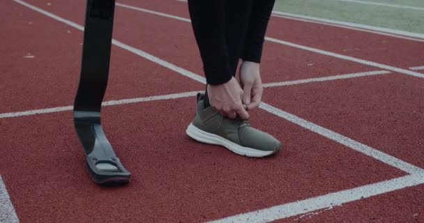 Crop view of disabled male person with prosthetic running blades tying shoelaces and standing at sports field. Concept of motivational sports footage, handicap,paralympian. — Stock Video