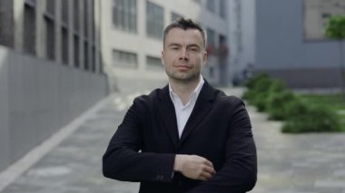 Yetişkin bir iş adamının kollarını kavuşturup kameraya bakması. 40 'lı yaşlarda, ofis binalarının yakınında dışarıda poz veren resmi kıyafetli bir adam portresi. İş kavramı. Yakınlaştır.