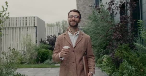 Crop view van gelukkige zakenman in glazen dragen lederen papieren map en koffie papieren beker. Baard stijlvolle man in halsdoek kijken opzij en glimlachen tijdens het lopen op straat. — Stockvideo