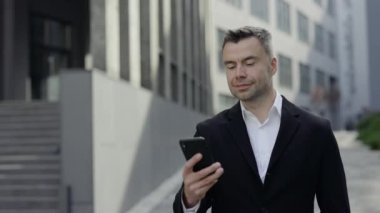 Resmi kıyafet giymiş neşeli yakışıklı bir adam. Telefon açarken konuşuyor. 40 'lı yılların CEO' su gülümserken akıllı telefondan konuşuyor ve sokakta yürüyor..