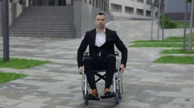 Tekerlekli sandalyede oturup giderken kameraya bakan takım elbiseli ciddi bir adamın portresi. Ofis binası yakınlarında 40 'lı yaşlarda engelli bir işadamı. Motivasyon kavramı.
