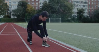 Ayakkabı bağcıklarını bağlayan protez koşu bıçakları olan engelli bir erkek. Spor sahasında bacağı kesilmiş bir adam. Motivasyon sporu görüntüsü kavramı.