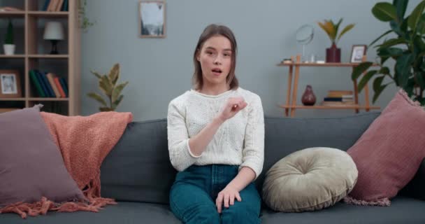Young woman saying nonverbal phrase I all understand while sitting on couch at home.Smiling female person looking to camera and communicating with deaf-mute sign language. — Stock Video