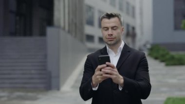 Klasik kıyafet giymiş neşeli, olgun iş adamının telefon ekranında mesaj yazışının görüntüsü. 40 'lı yaşlarda başarılı yakışıklı adam akıllı telefon kullanıyor ve sokakta yürürken gülümsüyor..