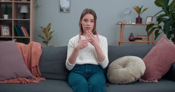 Jeune femme regardant à la caméra et montrant avec sourd-muet langage des signes sauver la planète. Femme attrayante ayant une déficience auditive soutenant le mouvement écologique tout en étant assise sur le canapé à la maison. — Video