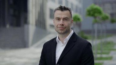 Kameraya bakan olgun iş adamının portresi. 40 'lı yaşlarda erkek, ofis binalarının yakınında açık havada poz verirken görüntülenmiş. İş kavramı ve başarılı. Yakınlaştır..