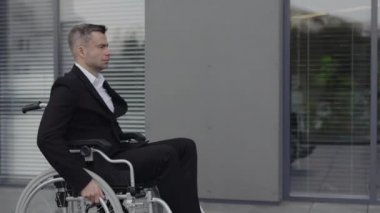 Sokakta yürürken tekerlekli sandalyedeki işadamının yan görüntüsü. Ofis binasının yakınında ciddi bir erkek yönetici var. Motivasyon kavramı, başarı.