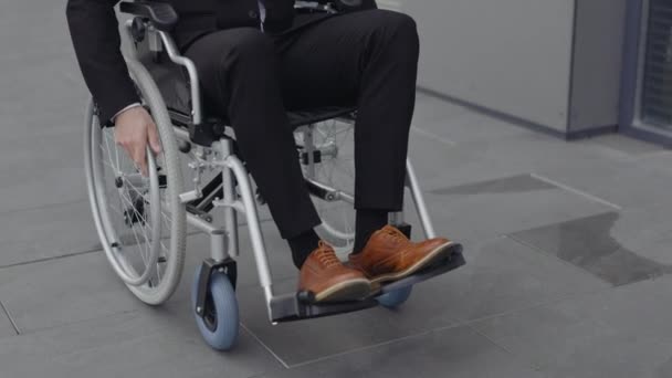 Вид на урожай бизнесмена в стильной обуви, идущего на инвалидной коляске на улице. Успешный мужчина едет на работу рядом с офисным зданием. Концепция мотивации, сетка. — стоковое видео