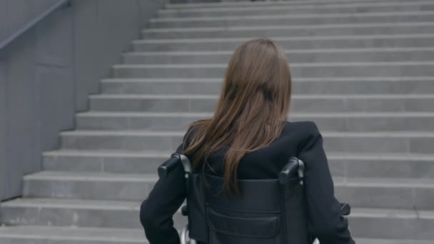 Vista posteriore della persona femminile in giacca e cravatta spingendosi sulla sedia a rotelle in strada. Donna disabile che va al lavoro e si ferma vicino alle scale degli uffici. Concetto di ostacoli, barriere. — Video Stock