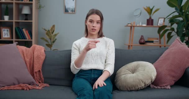 Millennial kvinna visar med dövstum teckenspråk säga nej till plast när du tittar på kameran. Attraktiv kvinnlig person som stöder eko rörelse medan du sitter på soffan hemma. — Stockvideo