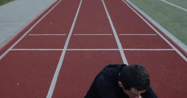 Spor sahasında otururken protez koşu bıçaklarıyla gerinen engelli genç adam. Antrenman elbisesi içinde bacağı kesilmiş bir erkek ısınıyor ve egzersiz yapıyor.. — Stok video