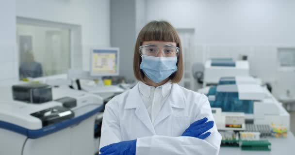 보호 웹 사이트와 의료용 마스크를 쓰고 카메라를 찾는 여성의 모습. 실험실에서 있는 동안 흰색 외투를 입고 팔짱을 끼고 있는 여성의 모습. — 비디오